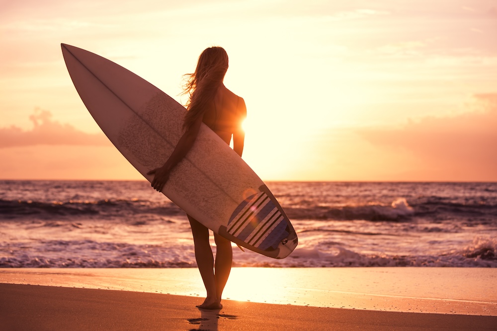 Silhouette surfer girl on the beach at sunset